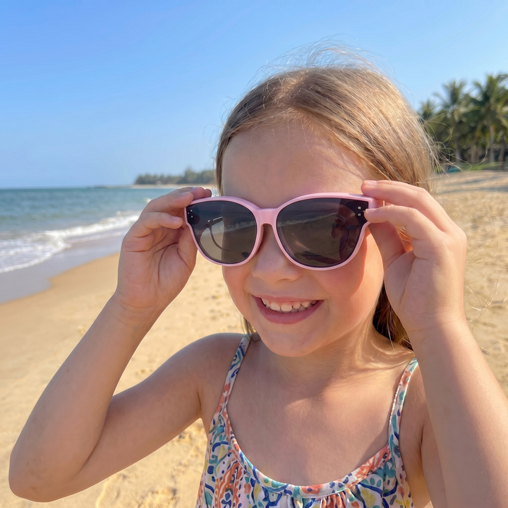 Smilende jente på stranden med rosa SunFit barnesolbriller